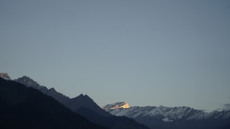 A panoramic view of a mountain range with hikers reaching the summit at golden hour.