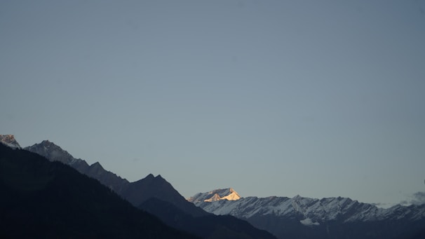 A panoramic view of a mountain range with hikers reaching the summit at golden hour.