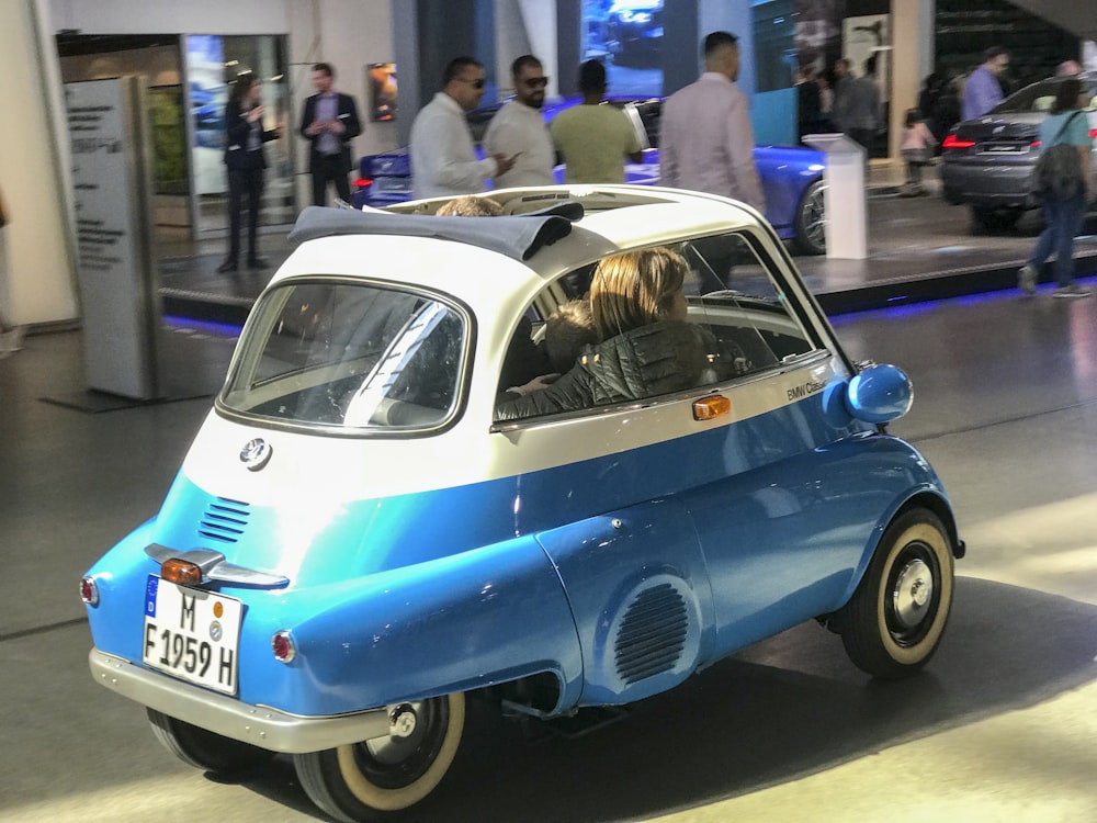 Une petite voiture bleue et blanche exposée dans un salon de l’auto