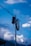 A utility pole with a coiled cable and a cylindrical transformer is set against a backdrop of a vibrant blue sky with scattered clouds. A mountainous landscape with snow-capped peaks is visible in the distance.