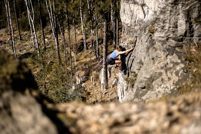 Close-up of climber gripping a rock face with safety gear in a forested area.