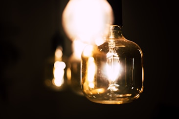 A close-up view of several glowing light bulbs hanging in a dark setting, emphasizing their warm light and transparent glass surfaces.