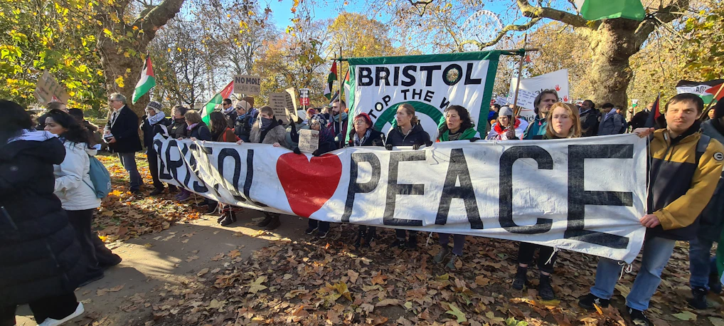 A vibrant crowd gathered in a sunny park, holding colorful peace banners during Delaware's Peace Week.