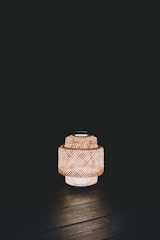 A woven lantern emits warm light against a dark background, creating a cozy and tranquil ambiance. The detailed lattice pattern of the lantern is clearly visible.