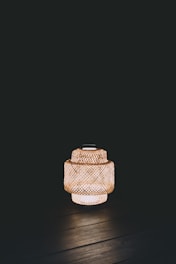 A woven lantern emits warm light against a dark background, creating a cozy and tranquil ambiance. The detailed lattice pattern of the lantern is clearly visible.