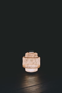 A woven lantern emits warm light against a dark background, creating a cozy and tranquil ambiance. The detailed lattice pattern of the lantern is clearly visible.