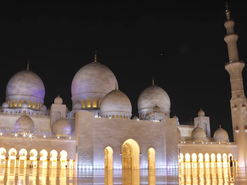 The intricate architecture of Sultan Qaboos Grand Mosque illuminated softly against the night.
