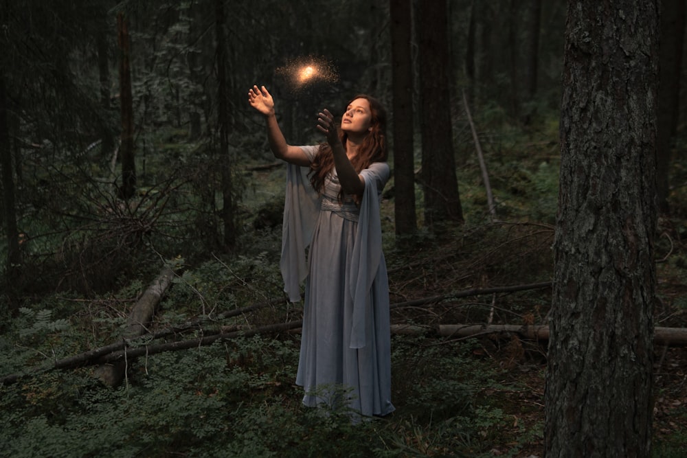 a woman standing in a forest holding a light in her hand