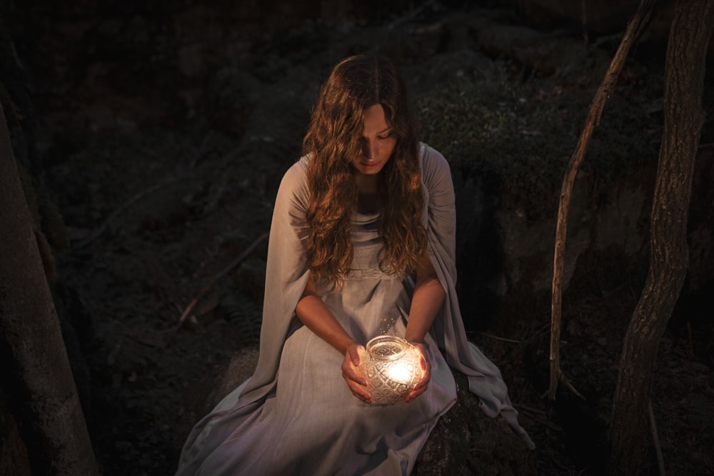 a woman sitting in the woods holding a candle