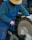 A person wearing blue overalls and a grey sweater operates a large circular grinding wheel. They are wearing a straw hat and appear to be focused on the task.