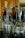 A collection of upside-down wine glasses and beverage bottles, including a champagne bottle with a golden foil wrapping on top. The glasses and bottles are placed on a dark surface in front of a wooden paneled background, creating reflections and playing with light and shadows.