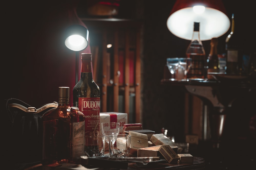 a table topped with a bottle of wine next to a lamp