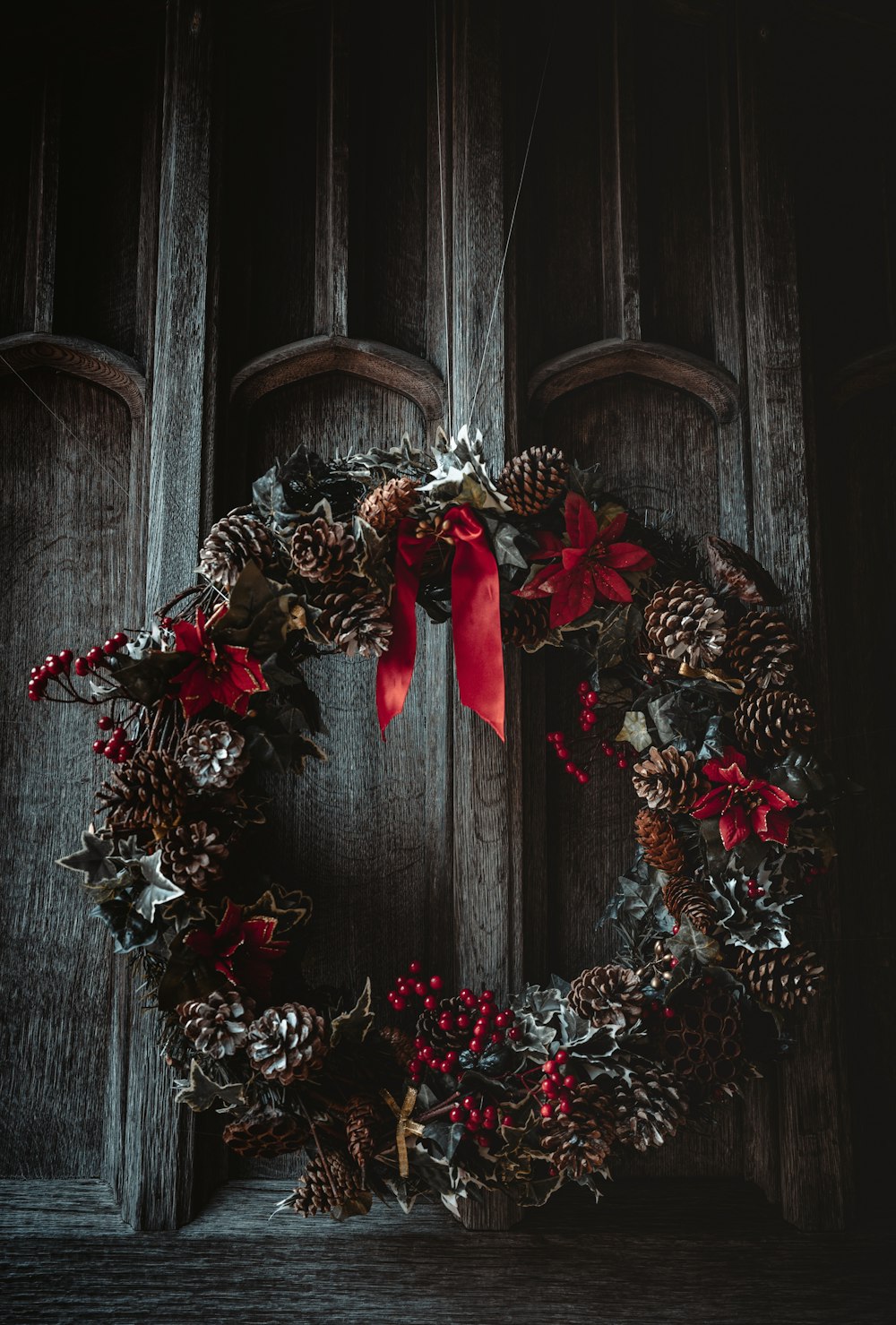 uma coroa de flores em uma porta de madeira com um laço vermelho