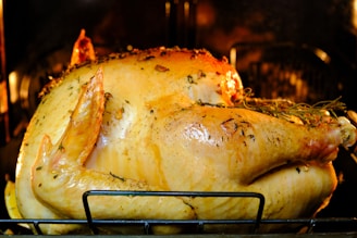 A golden brown roasted turkey is in the oven. The turkey is seasoned with herbs and spices, and its skin is slightly crispy and glistening. Rosemary and other herbs are visible on the surface, giving it a rustic and flavorful appearance.