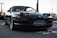 A sleek, dark-colored BMW sports car with pop-up headlights is parked in an outdoor setting. The car's license plate reads 'AUTOCULT,' and it is positioned on a paved area. The background reveals a gathering of vehicles and people, possibly at a car show or meetup.