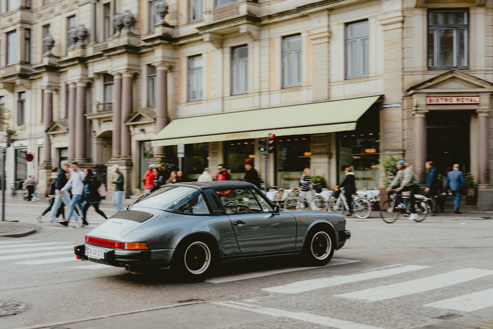 a grey car driving down a street next to tall buildings