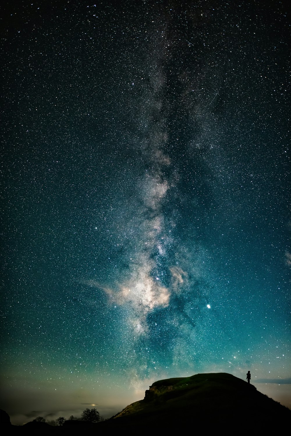 a person standing on top of a hill under a night sky