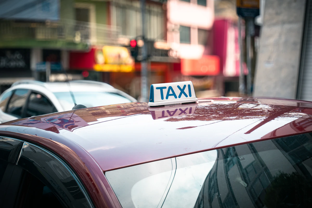 Un lumineux TAXI bleu et blanc posé sur le toit d'une voiture rouge, devant une rue commerçante floue
