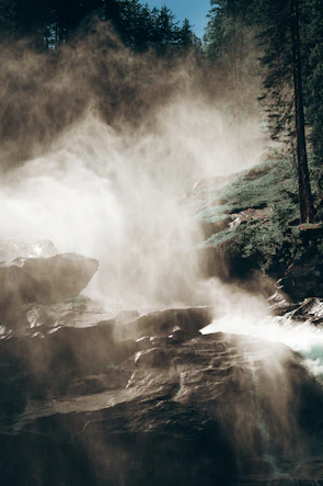 Sunset light illuminating a misty waterfall surrounded by dense forest.