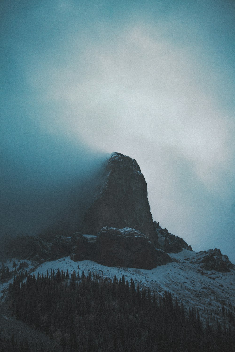 a mountain covered in snow and fog under a cloudy sky
