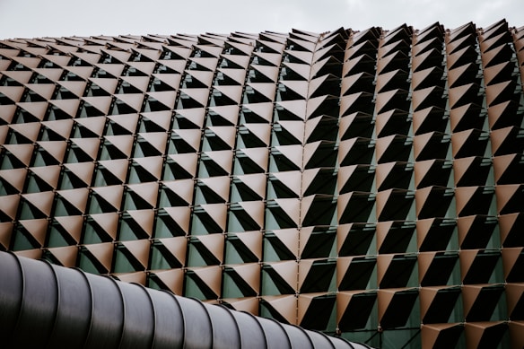 An architectural structure with a repeating pattern of triangular, metallic panels, each forming a geometric, spiky surface. The panels create a honeycomb-like texture that is both modern and visually striking.
