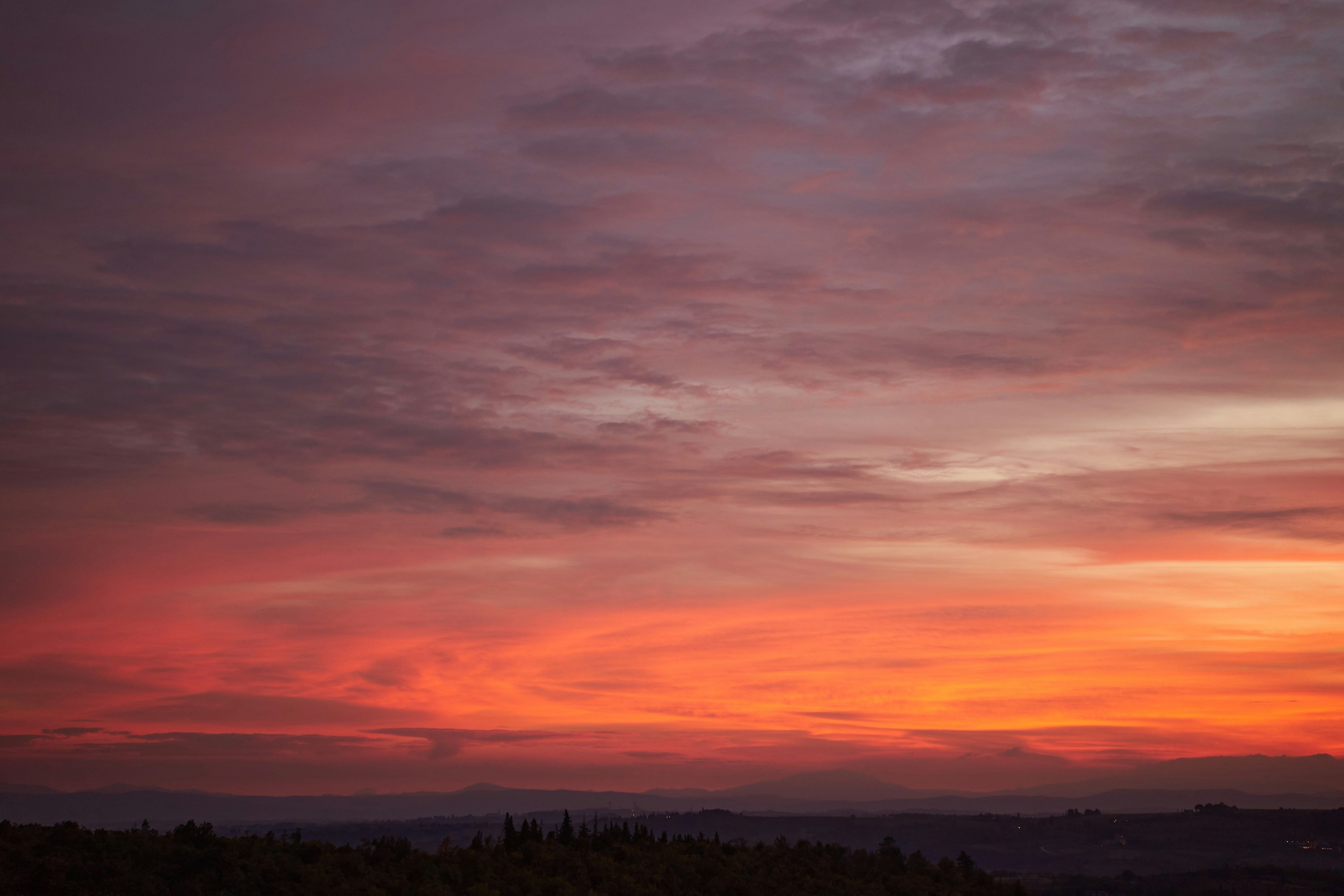 a sunset with clouds and trees in the foreground