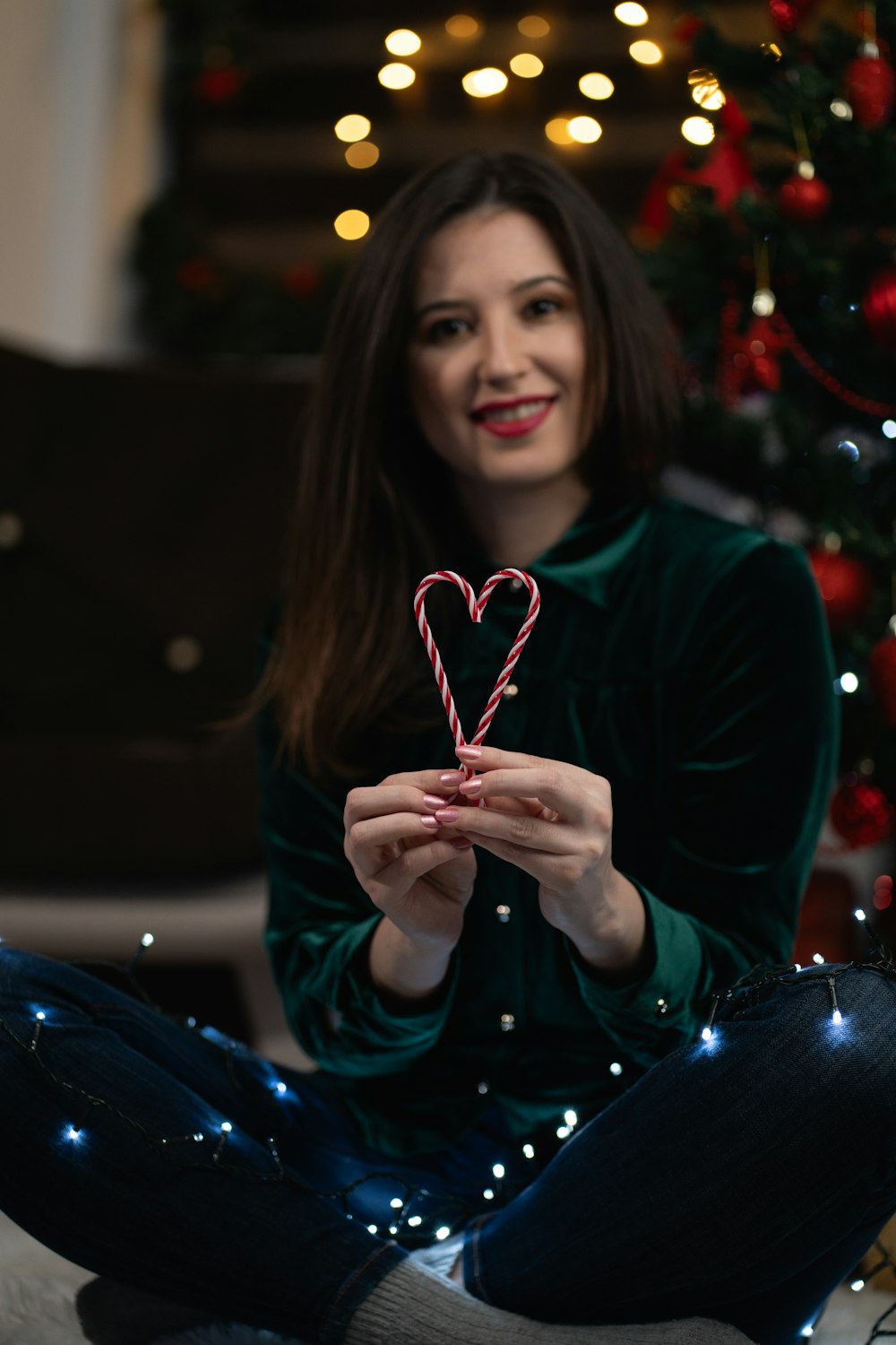 a woman holding a candy cane in front of a christmas tree