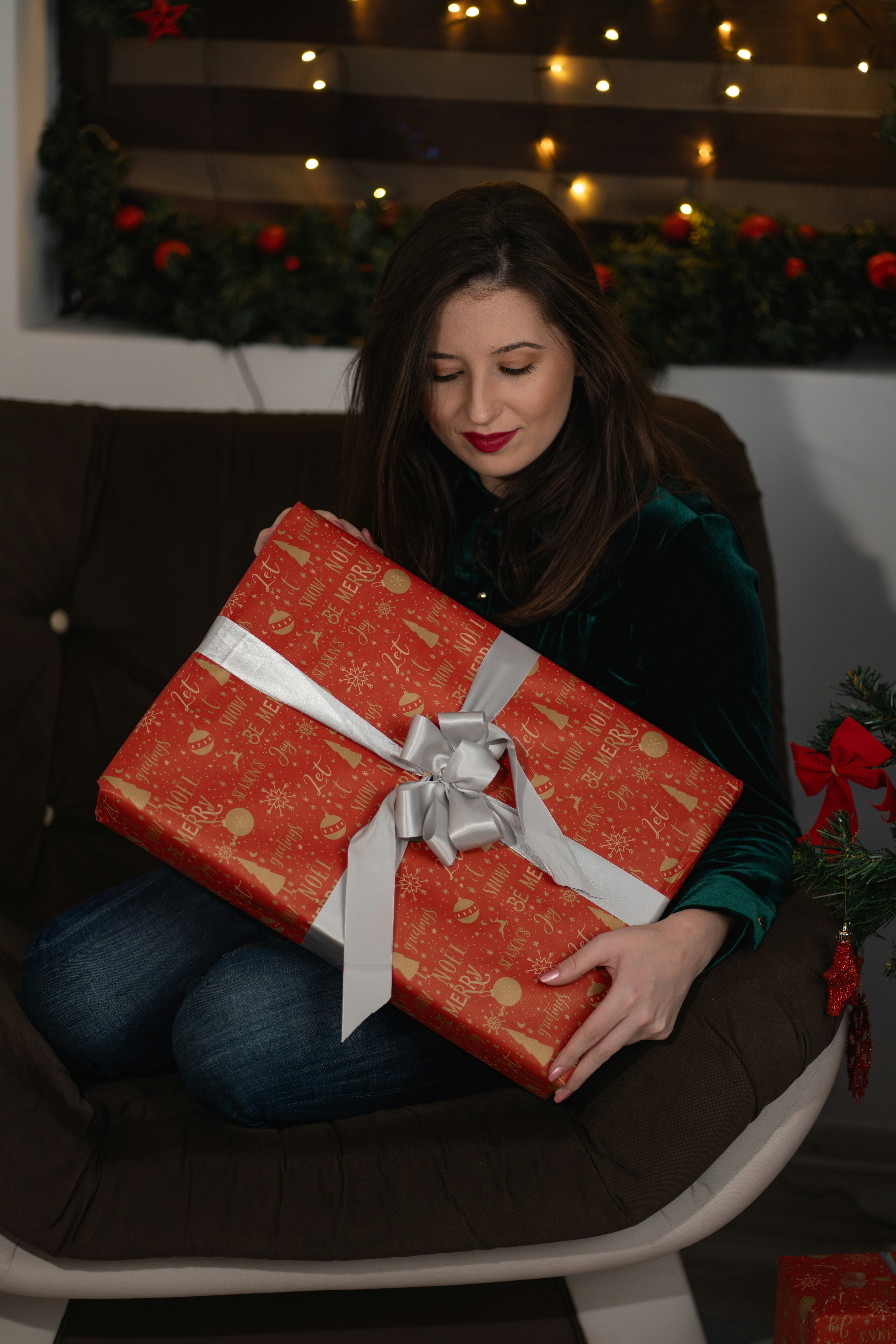 A happy woman holding a beautifully wrapped gift in a cozy living room.