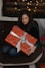 Photo of a smiling woman holding a beautifully wrapped gift box in a cozy living room.