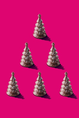 Six chocolate Christmas tree-shaped confections are arranged in a triangular pattern on a bright pink background. Each treat is dusted with powdered sugar, adding a festive touch.