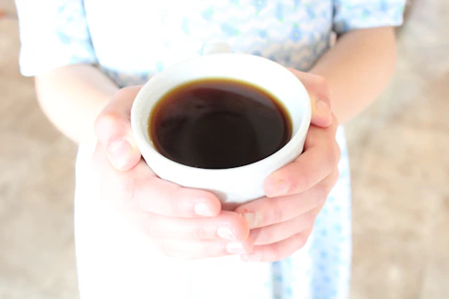 Elegant hands holding a ceramic cup with swirling coffee vapor rising gently.