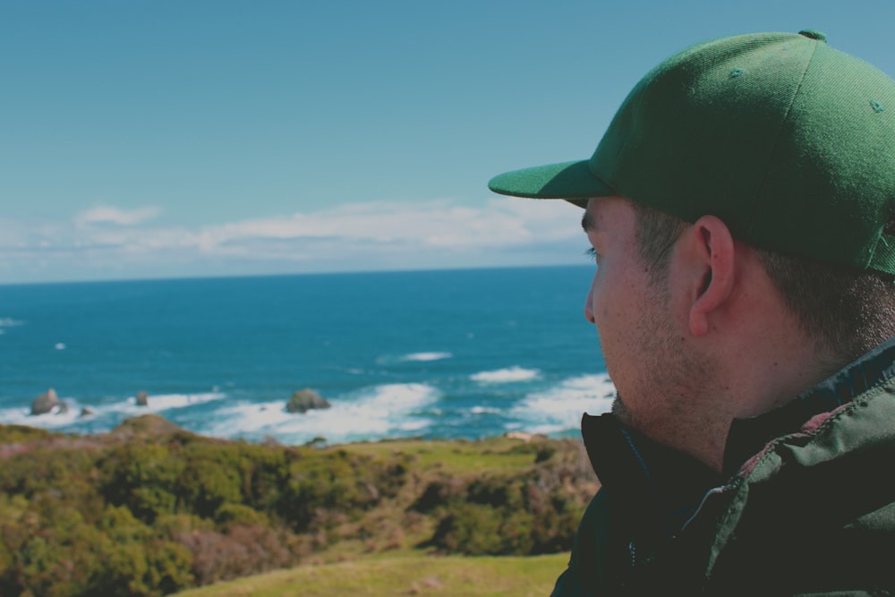 a man wearing a green hat looking out at the ocean