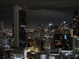Nighttime city skyline with illuminated skyscrapers representing international financial hubs.