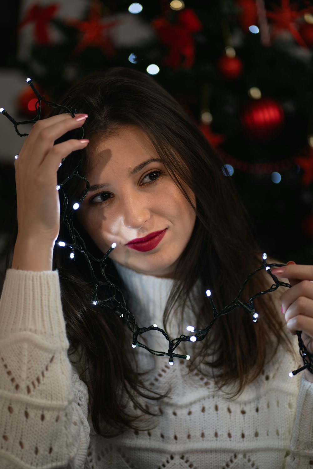 a woman holding a string of lights in front of a christmas tree