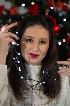 A smiling mom holding a filled Christmas stocking with twinkling lights in the background.