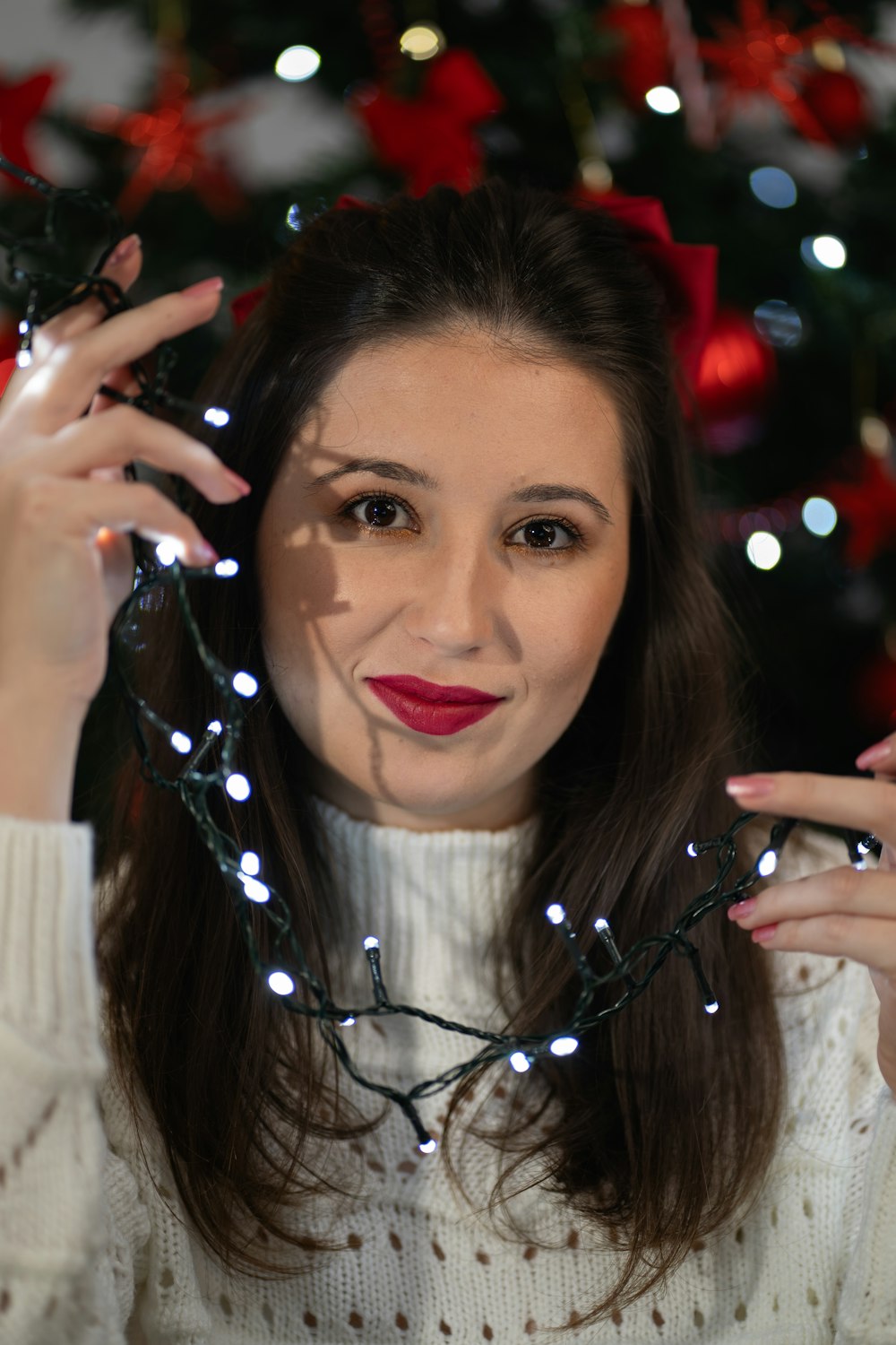a woman wearing a white sweater holding a string of christmas lights