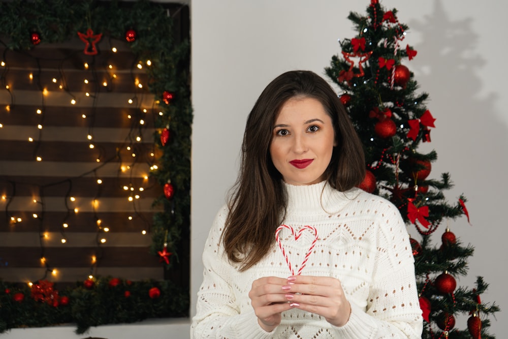 a woman in a white sweater holding a candy cane in front of a christmas tree