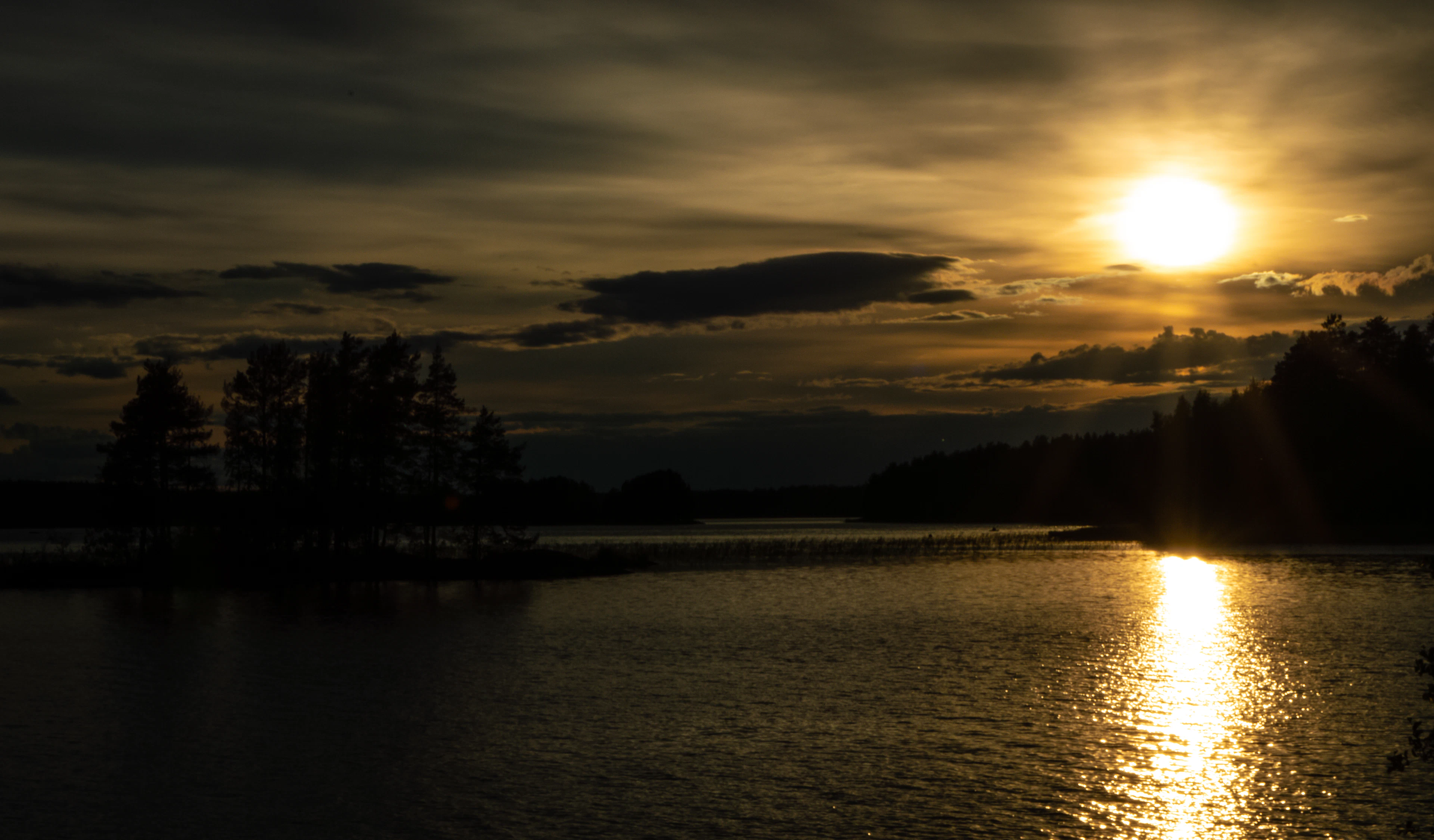 Low evening sun over a calm Finnish lake and the silhouettes of wooded islets