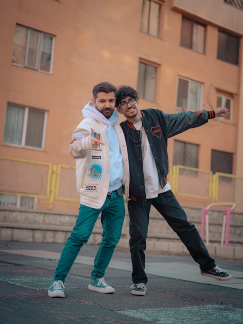 A candid shot of two friends laughing, dressed in layered unisex jackets and relaxed-fit jeans, walking through a sunlit urban street.