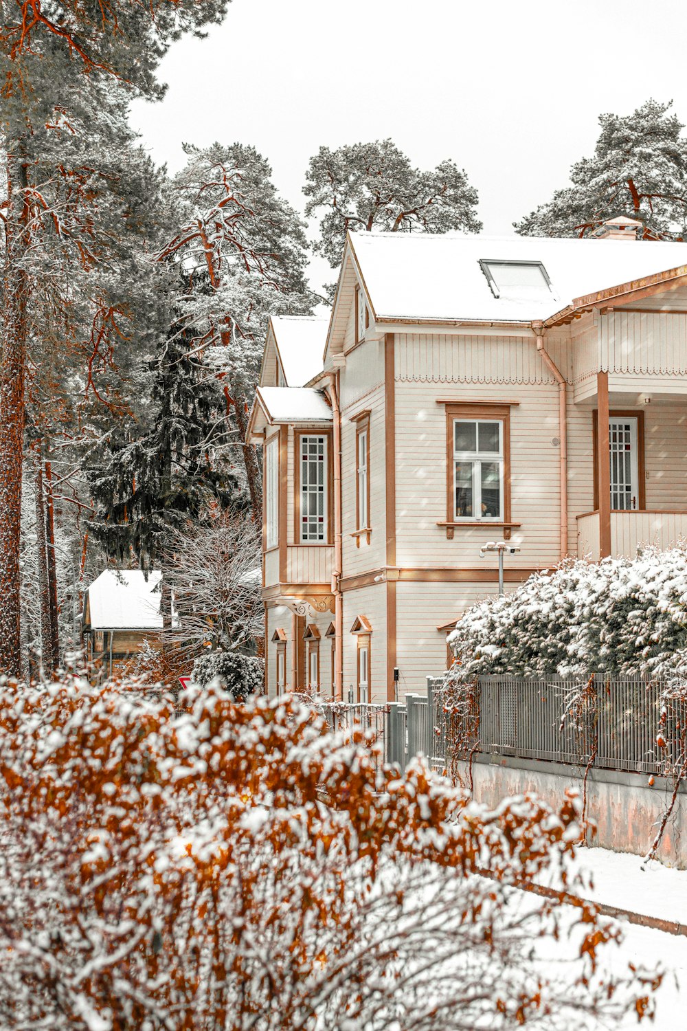 a snow covered house with a fence and trees in the background