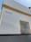 A corner of a white building with yellow trim is visible. The word 'BRASIL' is written on the wall. There is a window with a black decorative wrought iron grill on the right side, framed in yellow.