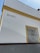 A corner of a white building with yellow trim is visible. The word 'BRASIL' is written on the wall. There is a window with a black decorative wrought iron grill on the right side, framed in yellow.