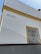 A corner of a white building with yellow trim is visible. The word 'BRASIL' is written on the wall. There is a window with a black decorative wrought iron grill on the right side, framed in yellow.