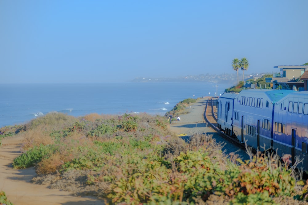 a blue train traveling down tracks next to the ocean