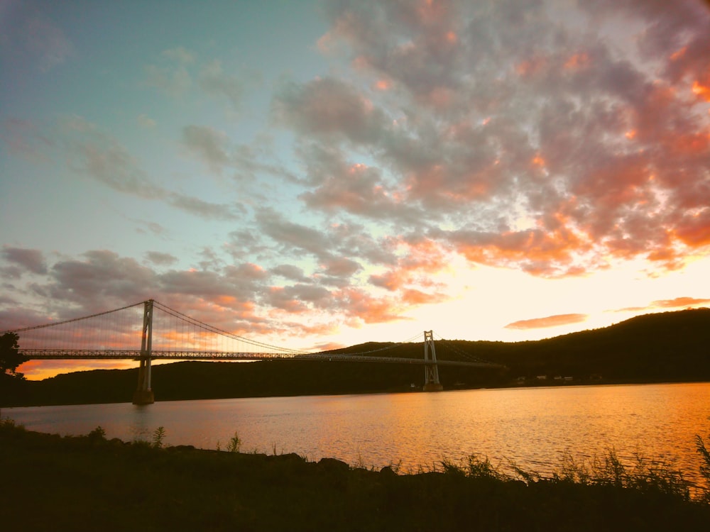 the sun sets over a bridge and a body of water