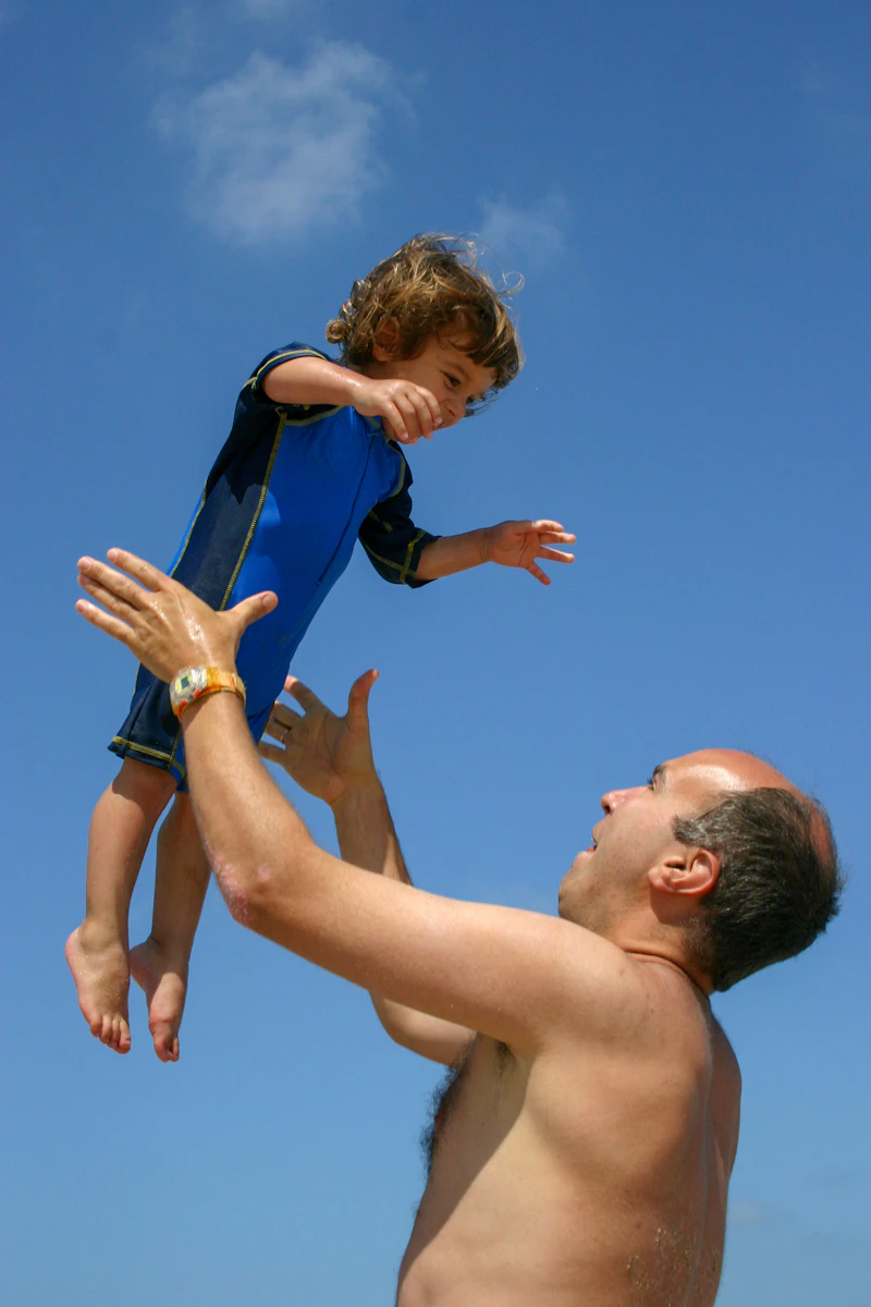 Father joyfully lifting his child up under a bright sunny sky