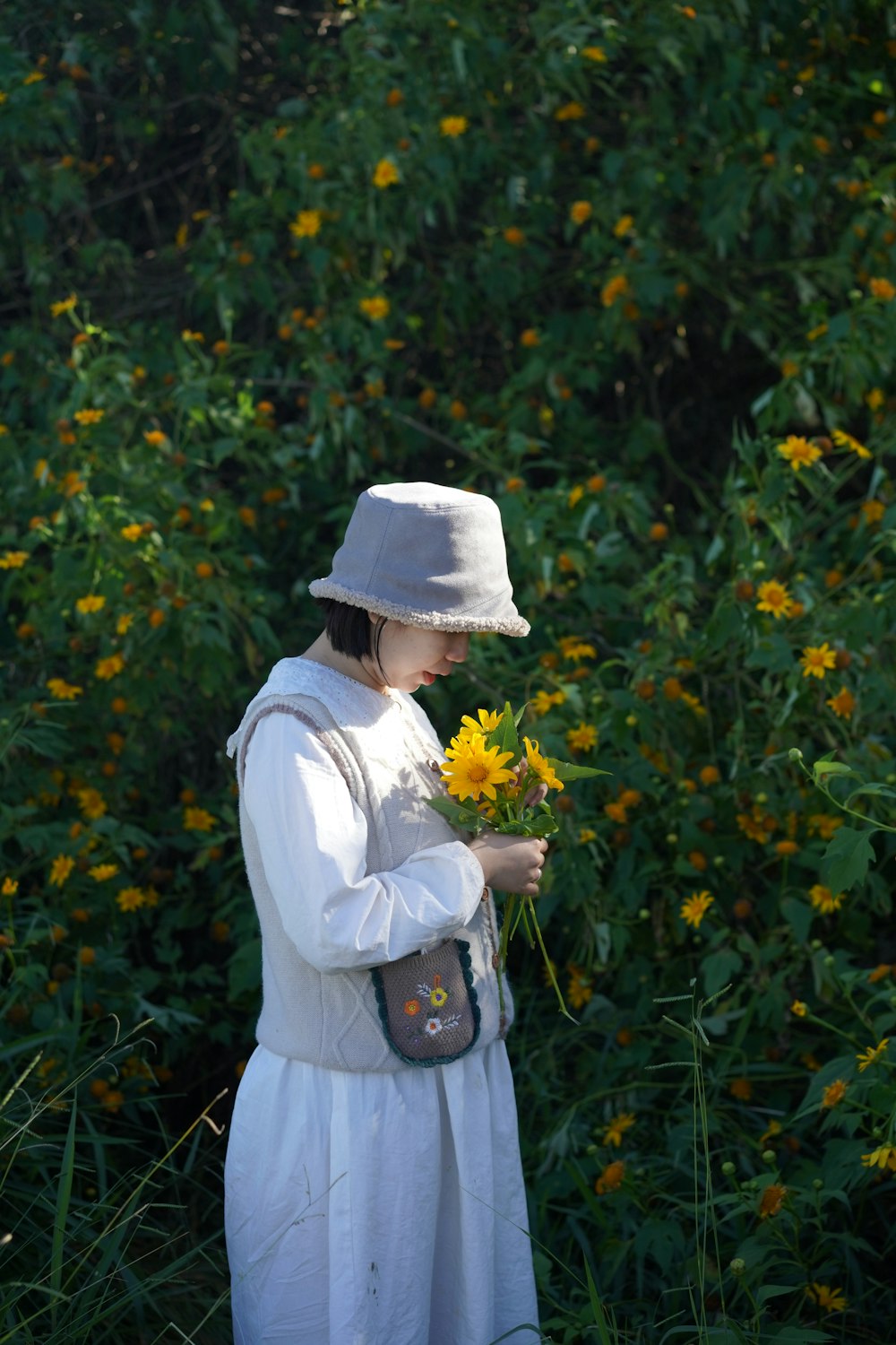 a woman in a white dress and hat holding a yellow flower