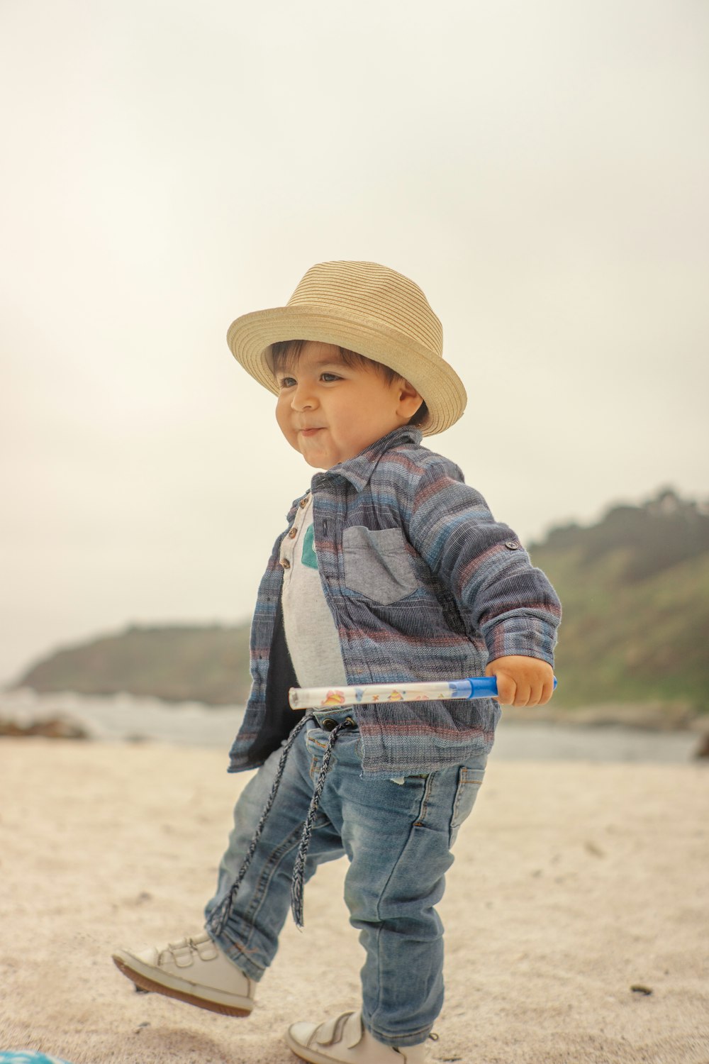 a little boy walking on a beach with a hat on