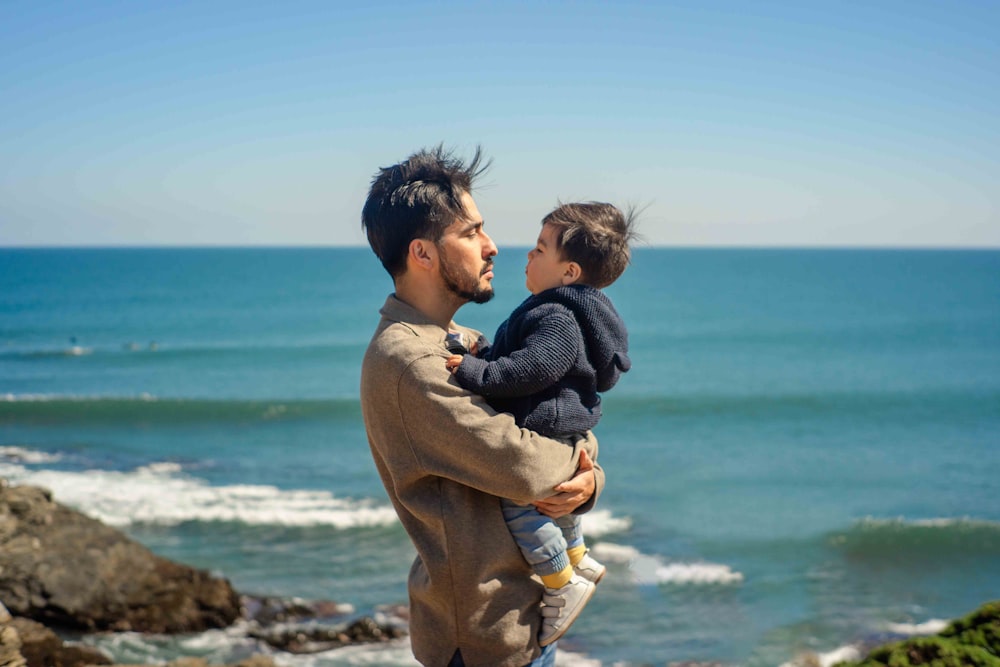a man holding a small child near the ocean