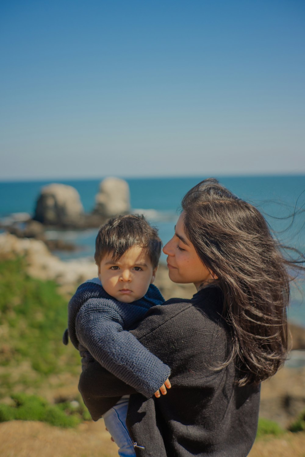 a woman holding a small child near the ocean